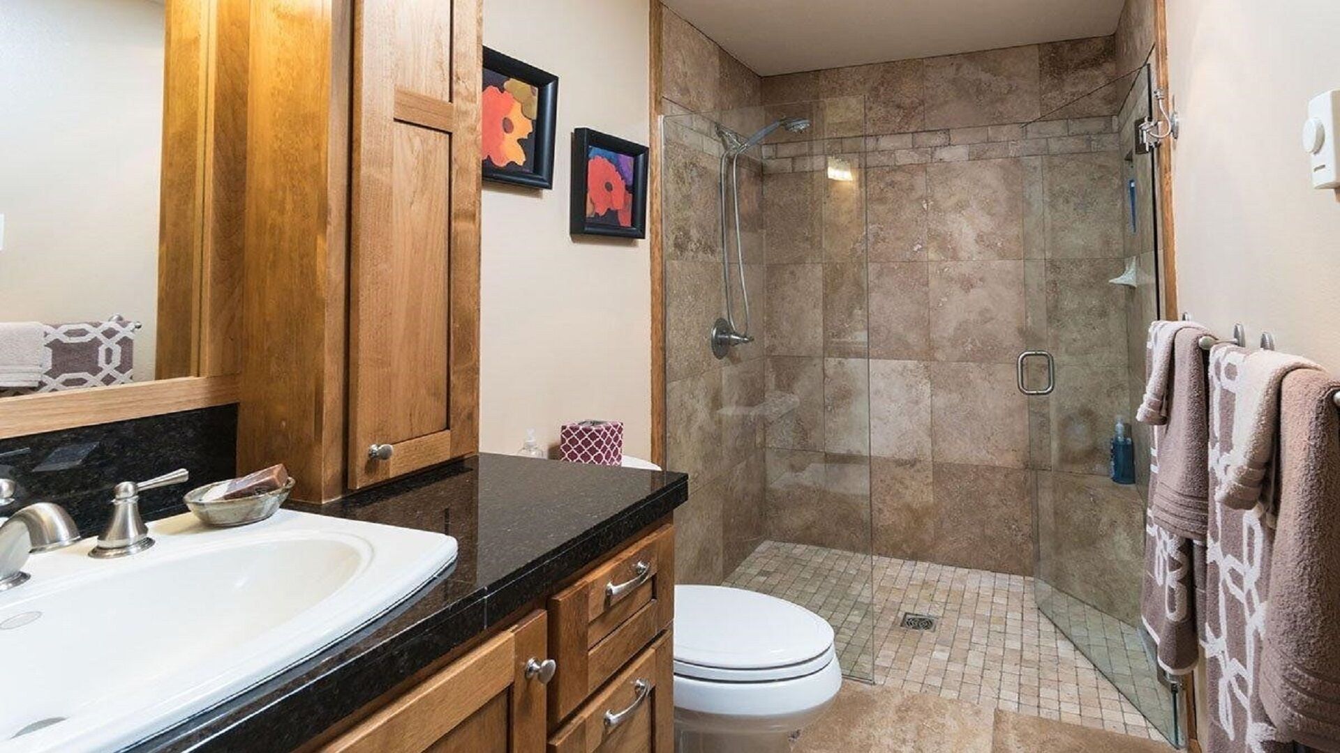 Un baño moderno con un lavabo de mármol, armarios de madera, cabina de ducha de vidrio y un inodoro.