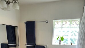 Un baño con inodoro blanco, lavamanos con encimera de granito, espejo y dos toallas colgadas en barras.