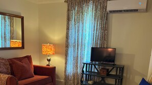 Una habitación de hotel con cama, sofá, televisor sobre un mueble, lámpara y cortinas.