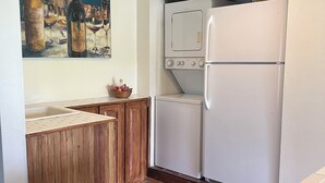 Una cocina con suelo de baldosas, armarios de madera, un refrigerador blanco y un cuadro con botellas de vino.