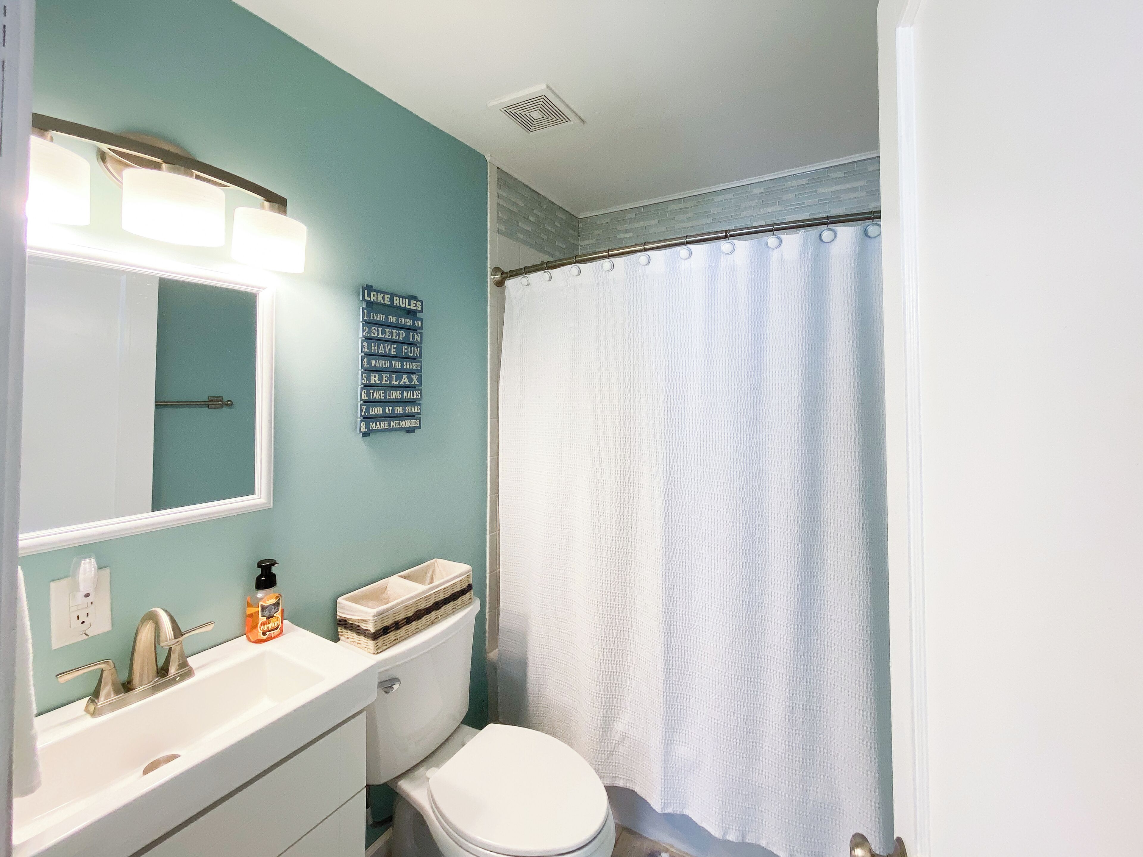 Un baño con un inodoro blanco, un lavabo con dispensador de jabón y un espejo sobre el lavabo.