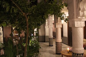 A traditional interior with ornate columns, a wooden table with a candle, and lush greenery.