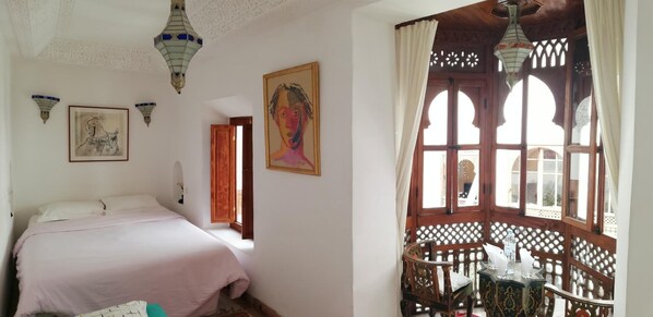 A bedroom with a bed, a painting, and a window with a view.