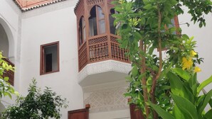 A courtyard with a wooden balcony, a large archway, and various plants and flowers.