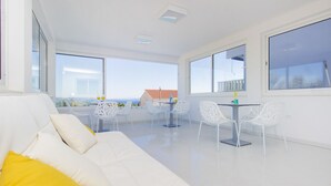 A modern, bright living room with a white sofa, yellow pillow, and a dining area with white chairs and a table. - Villa Tramonto (Seget)