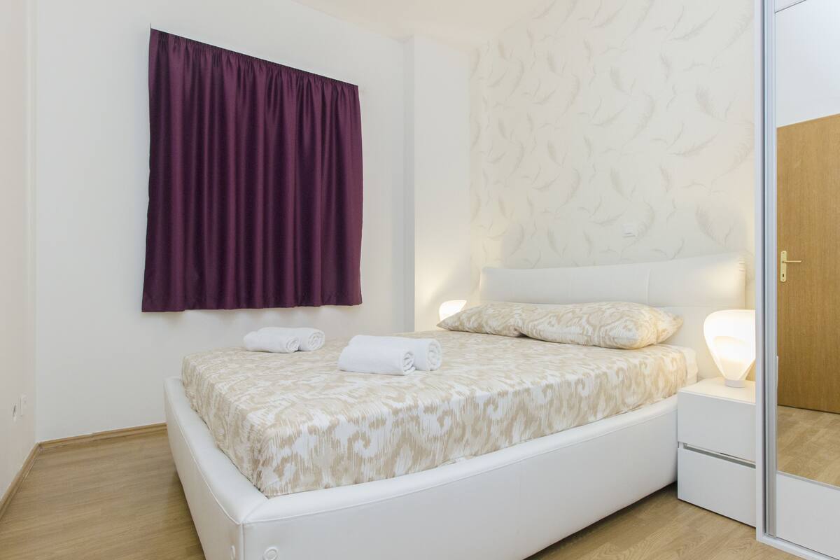 A modern bedroom with a bed, a nightstand, a wall-mounted curtain, and a patterned wall.