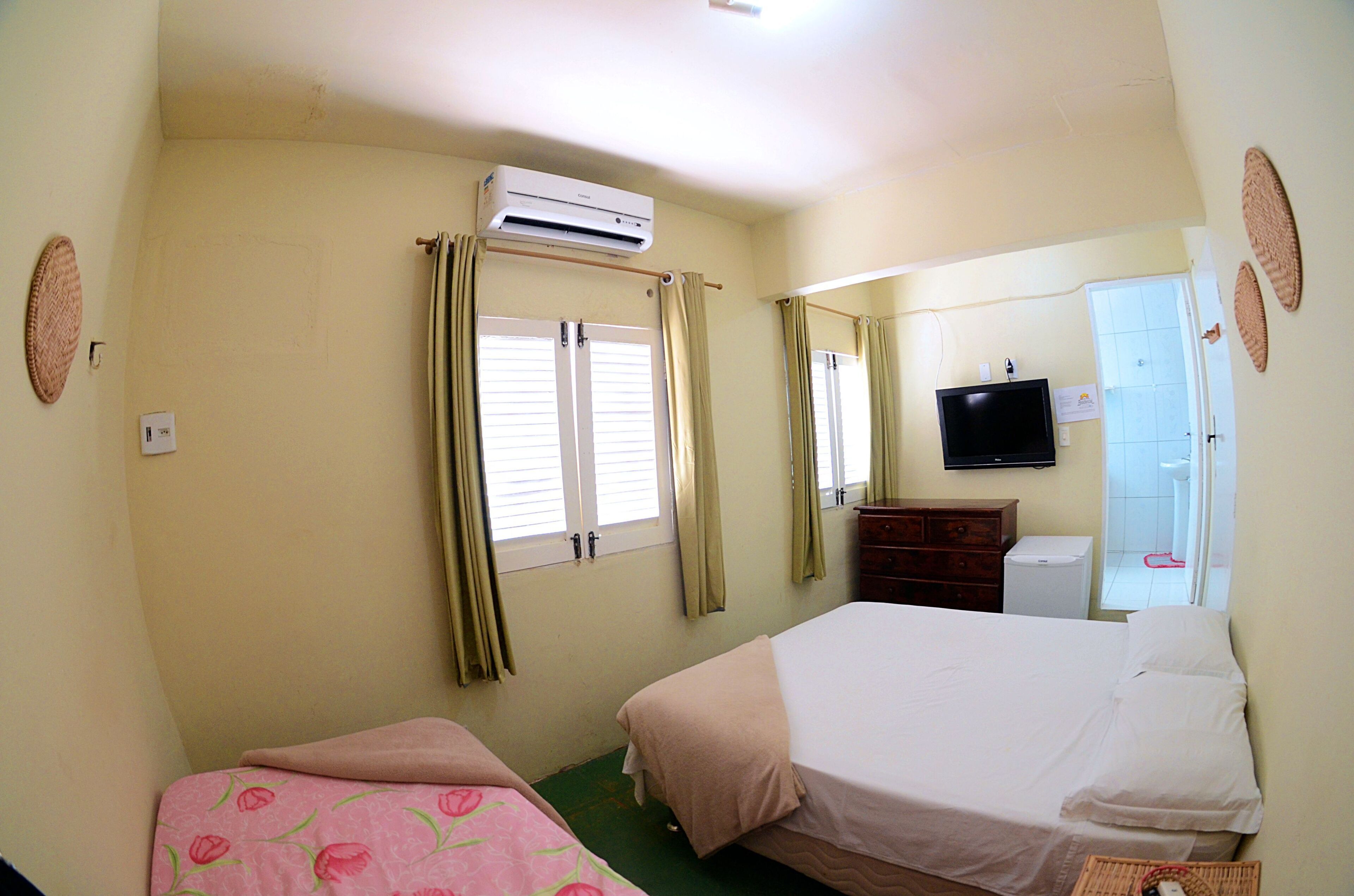A hotel room with two beds, an air conditioning unit, a television, and a bathroom visible through an open door.