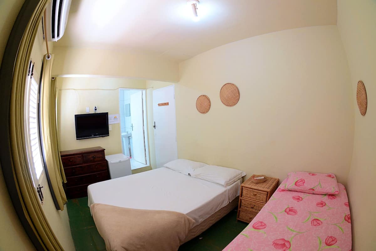 A bedroom with a bed, a dresser, a television, and a small table with a basket.