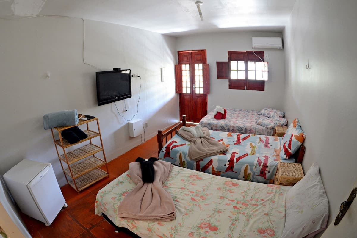 A room with two beds, a television, a small refrigerator, and a window with wooden shutters.
