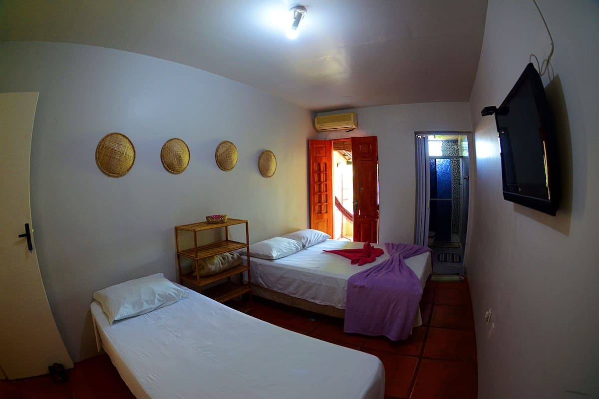 A small, simple room with two beds, a shelf with baskets, a television, and a door leading to another room.