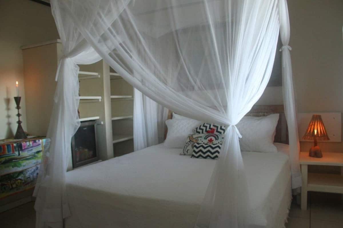 A bed with a canopy, a bedside table with a lamp, and a shelf with books and decorative items.