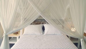 Una cama con un colchón blanco acolchado y almohadas blancas, bajo un dosel blanco.