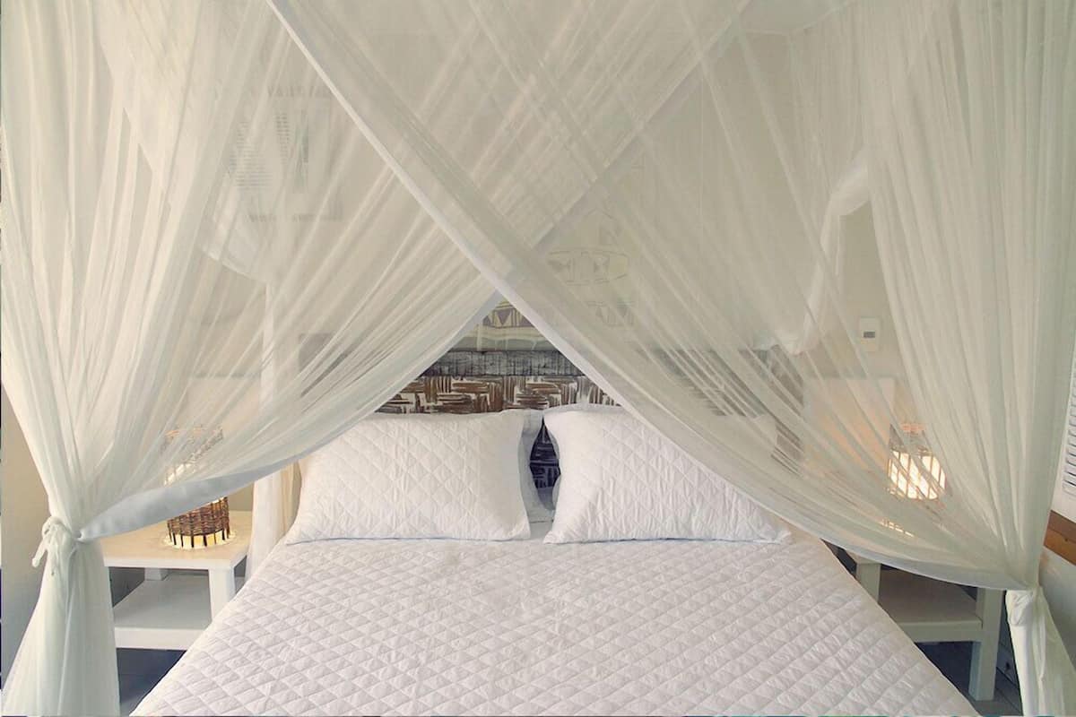 A bed with a white quilted mattress and white pillows, under a white canopy.