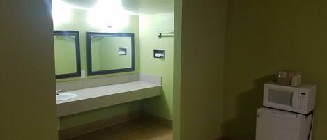 A small bathroom with a sink, two mirrors, a microwave, and a toilet.