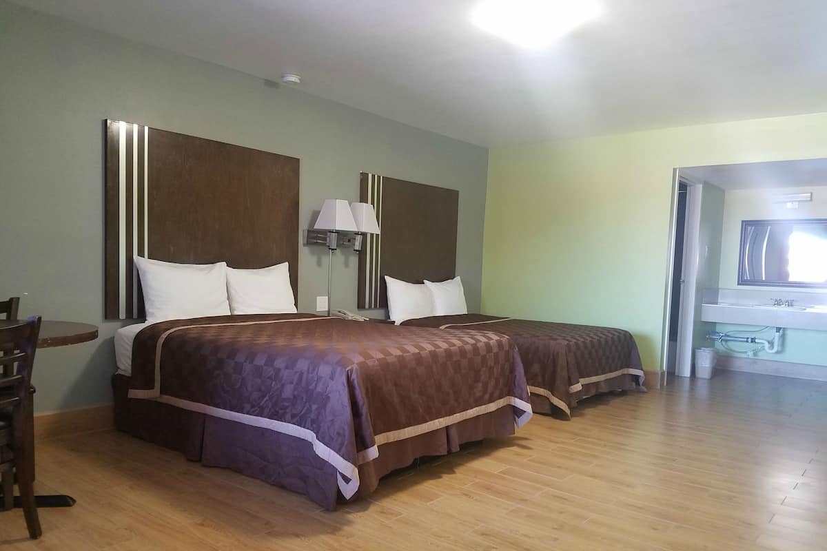 A hotel room with two beds, a desk, a chair, a lamp, and a bathroom visible through an open door.