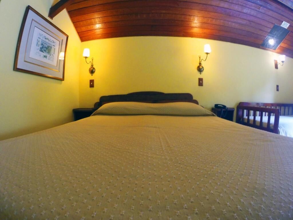A bedroom with a bed, two wall-mounted lamps, and a framed picture on the wall.