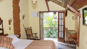 A room with a bed, a chair, a desk, and a balcony with a view of greenery. - Pousada Imperial Koeler (Petrópolis)