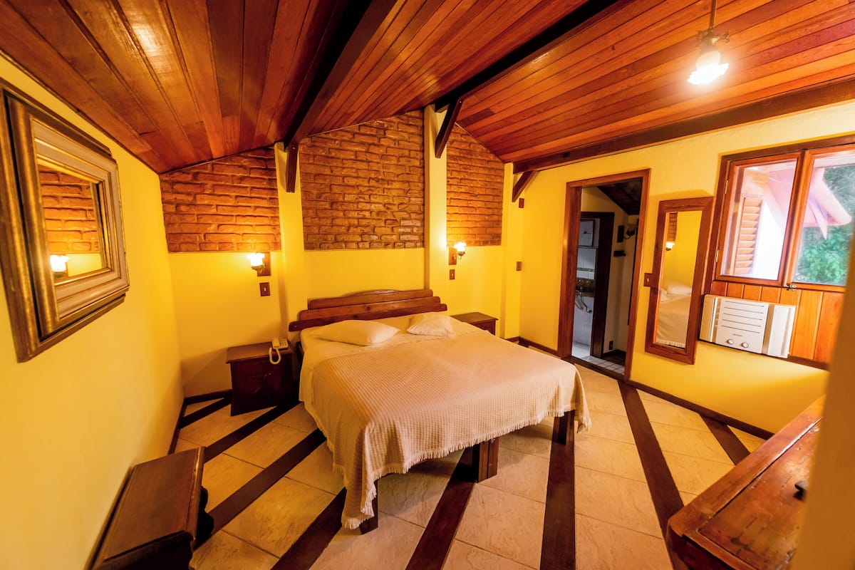 A bedroom with a wooden ceiling, a brick wall, and a bed with a white bedspread.