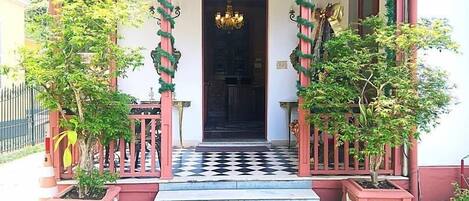 Entrada de edificio con suelo a cuadros, un candelabro y dos plantas en macetas a cada lado.