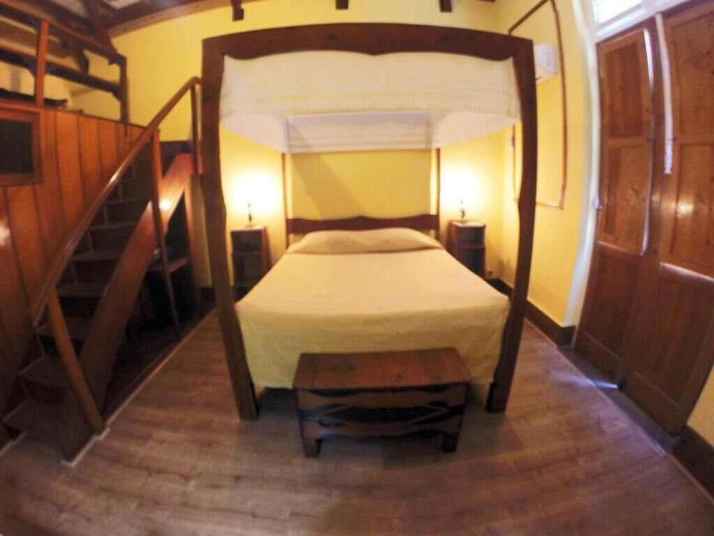 Et værelse med himmelseng, trægulv, en lille bænk og en trappe.
