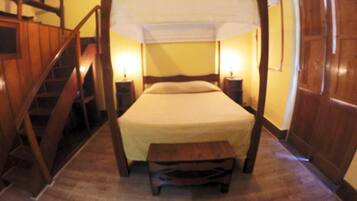 A room with a four-poster bed, wooden flooring, a small bench, and a staircase.