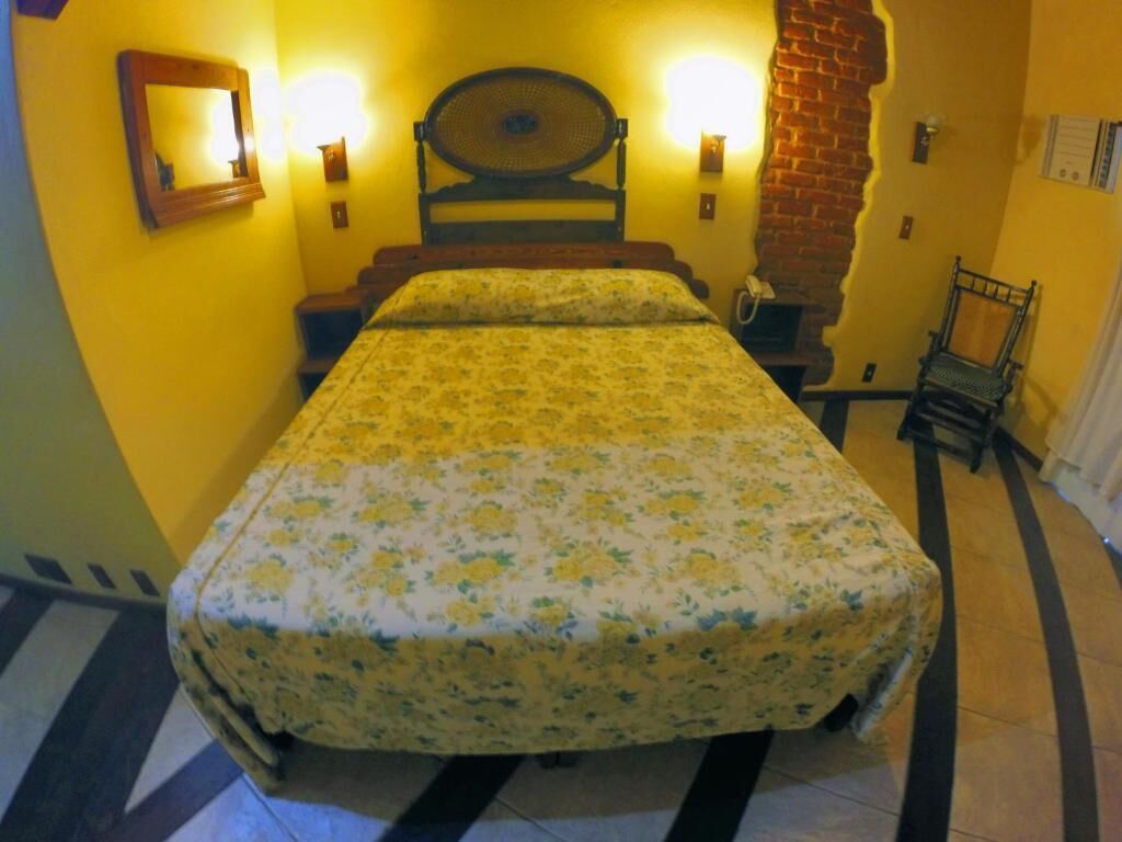 Un letto con copriletto floreale, due lampade a parete, una testiera in legno, un muro in mattoni e una sedia.