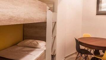 A compact room with a bunk bed, a small table with chairs, and a window with blinds.