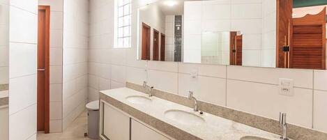 Un baño con tres lavamanos, un espejo grande y un cubo de basura.