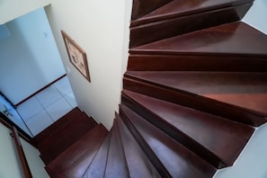 Una escalera de madera con barandilla que lleva a un cuarto con pared de color claro y un cuadro enmarcado.
