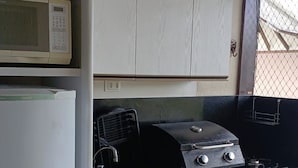 A compact kitchen with a microwave, a gas stove, and a sink. - Nannai Residence Apartments - Muro Alto (Porto de Galinhas - PE) (Ipojuca)