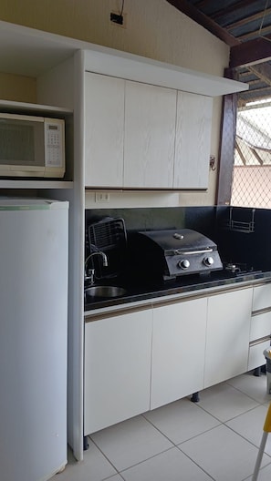 A compact kitchen with a microwave, a gas stove, and a sink. - Nannai Residence Apartments - Muro Alto (Porto de Galinhas - PE) (Ipojuca)