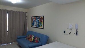 A living room with a blue sofa, a colorful painting on the wall, and a window with curtains.