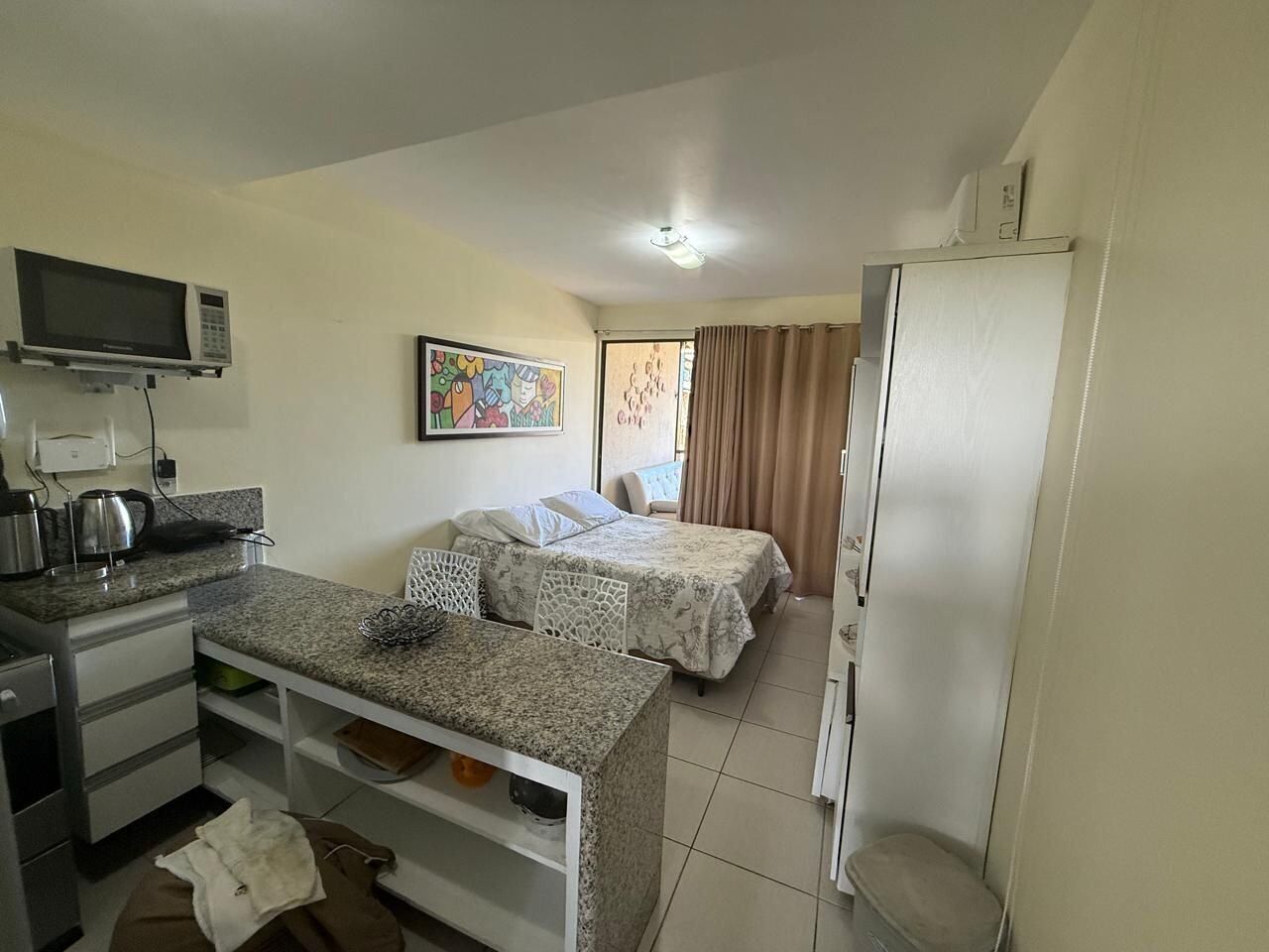 Quarto de hotel pequeno com cozinha compacta, duas camas, televisão e um quadro na parede.