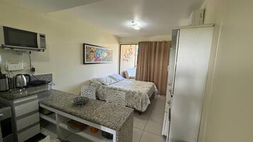 Quarto de hotel pequeno com cozinha compacta, duas camas, televisão e um quadro na parede.