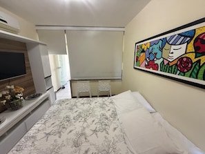 Une chambre à coucher avec un lit, une télévision, un bureau agrémenté d’un vase de fleurs et une peinture abstraite aux couleurs vives accrochée au mur.