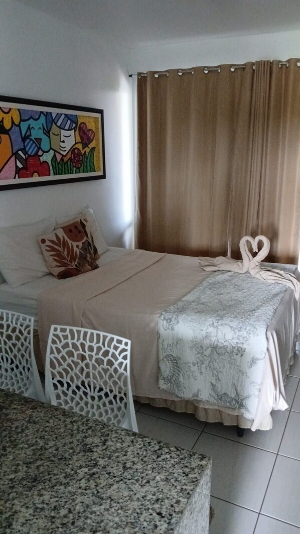 A hotel room with a bed, a table, chairs, a curtain, and a painting on the wall.