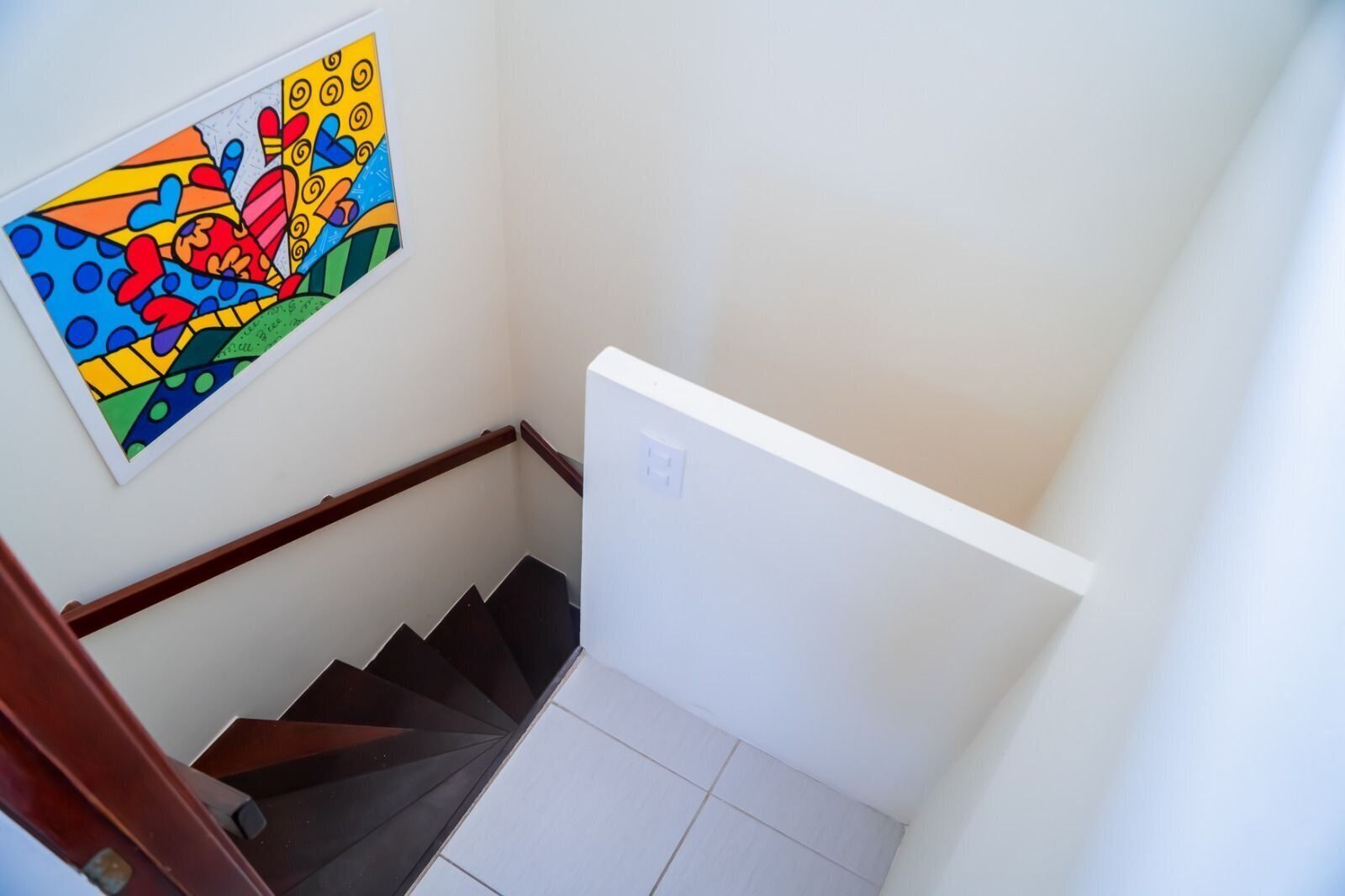 A staircase with a handrail, a wall-mounted colorful artwork, and a light switch.