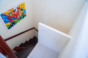 Un escalier avec une rampe, une œuvre d’art colorée accrochée au mur et un interrupteur.