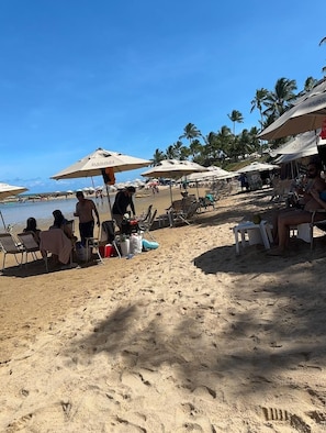 Una playa con tumbonas y sombrillas, palmeras y cielo despejado.