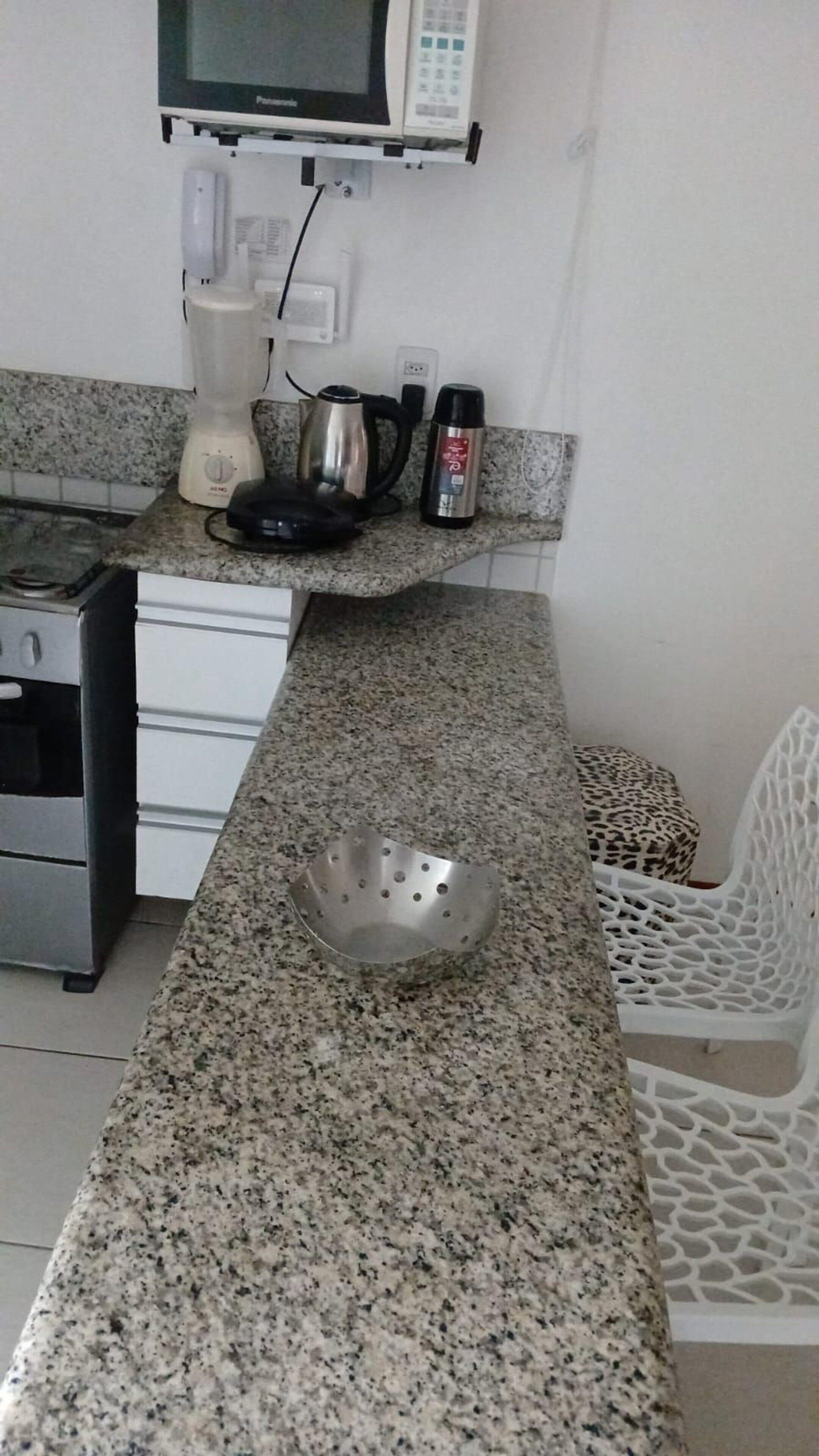 A kitchen with granite countertops, a stainless steel kettle, a blender, and a microwave.
