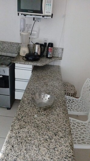 A kitchen with granite countertops, a stainless steel kettle, a blender, and a microwave.