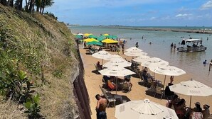 A beachside area with rows of umbrellas and beach chairs, a sandy path, and a view of the sea. - Nannai Residence Apartments - Muro Alto (Porto de Galinhas - PE) (Ipojuca)