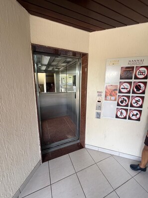 Un ascensor con puerta de vidrio, un cartel con artículos prohibidos y suelo de baldosas.