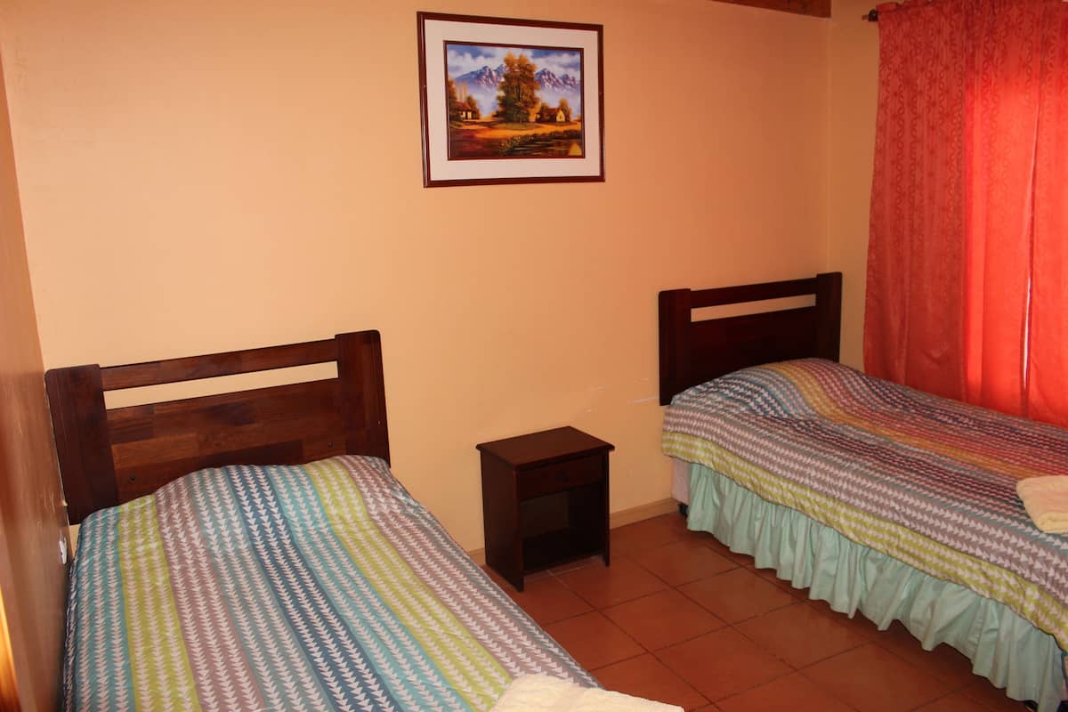 A room with two single beds, a small bedside table, a framed picture on the wall, and a red curtain.