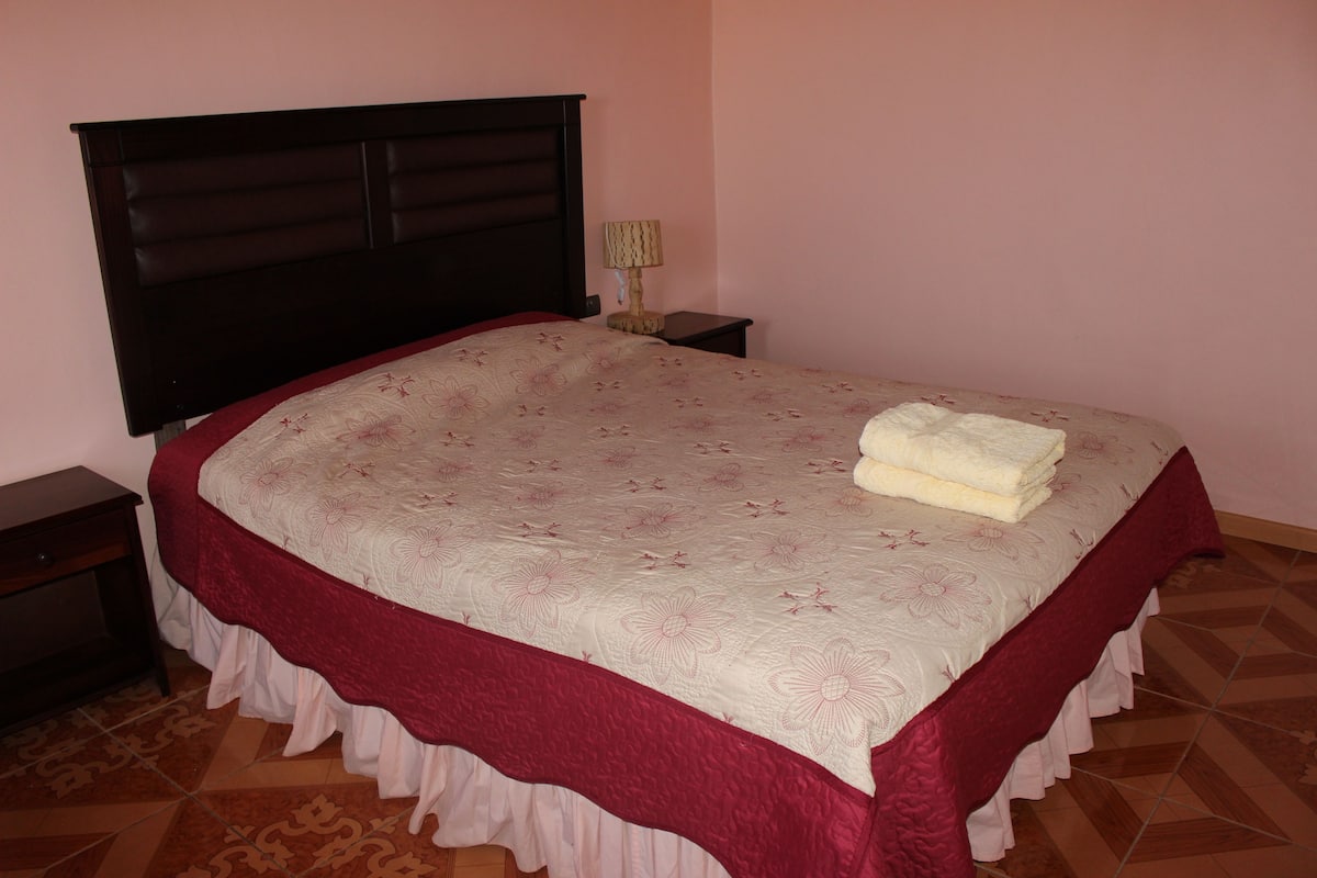 A neatly made bed with a floral bedspread and a red skirted bed skirt.