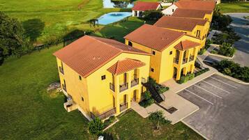 A yellow building with red roofs, a parking lot, and a small pond.