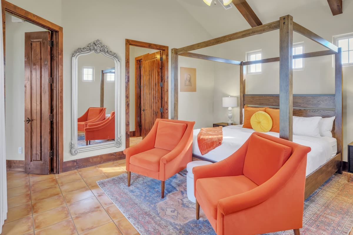 A bedroom with a four-poster bed, two orange armchairs, a large mirror, and a wooden ceiling.
