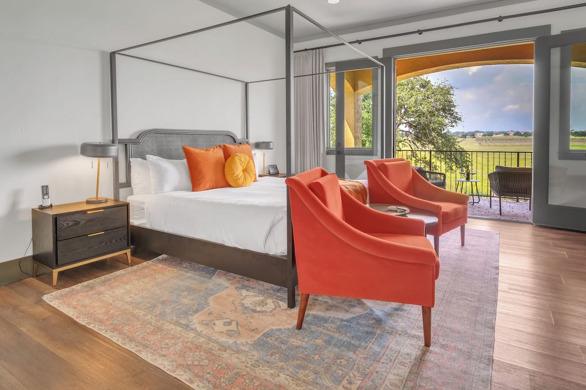 A modern bedroom with a four-poster bed, a large window with a view of the countryside, and a balcony with outdoor seating.