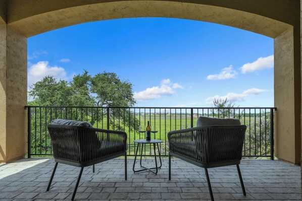 A balcony with two wicker chairs and a small table, overlooking a green landscape.