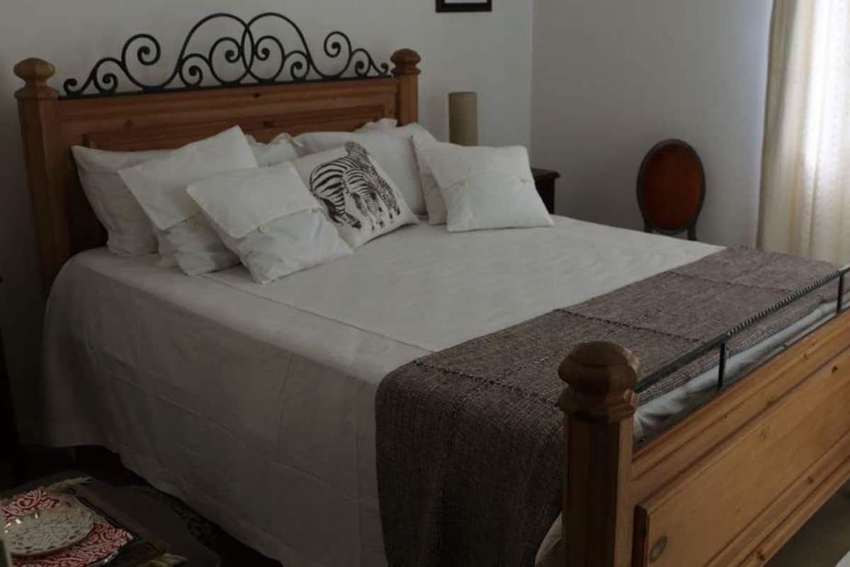 Une chambre avec un lit en bois, une literie blanche et un plaid à motifs.